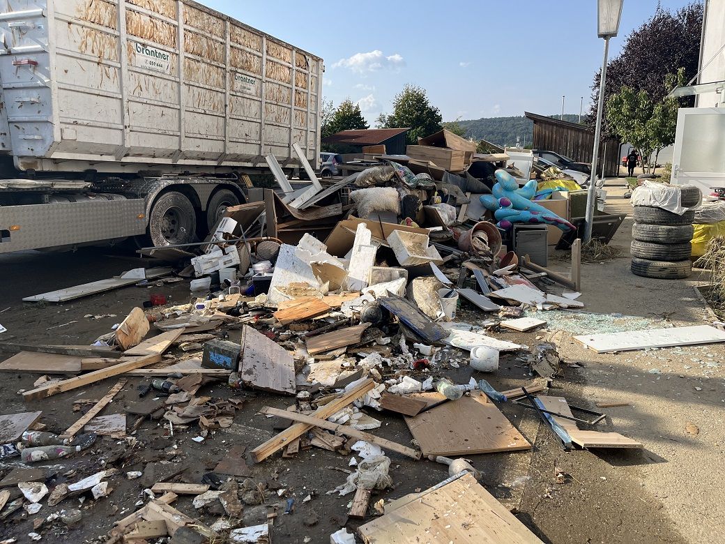 Hochwasser-Sperrmüll, Autoreifen etc. liegt auf der Straße, LKW der Fa. Brantner im Hintergrund