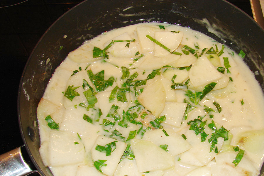 Kohlrabistücke in weißer Sauce garniert mit Kräutern in einer schwarzen Stielpfanne.