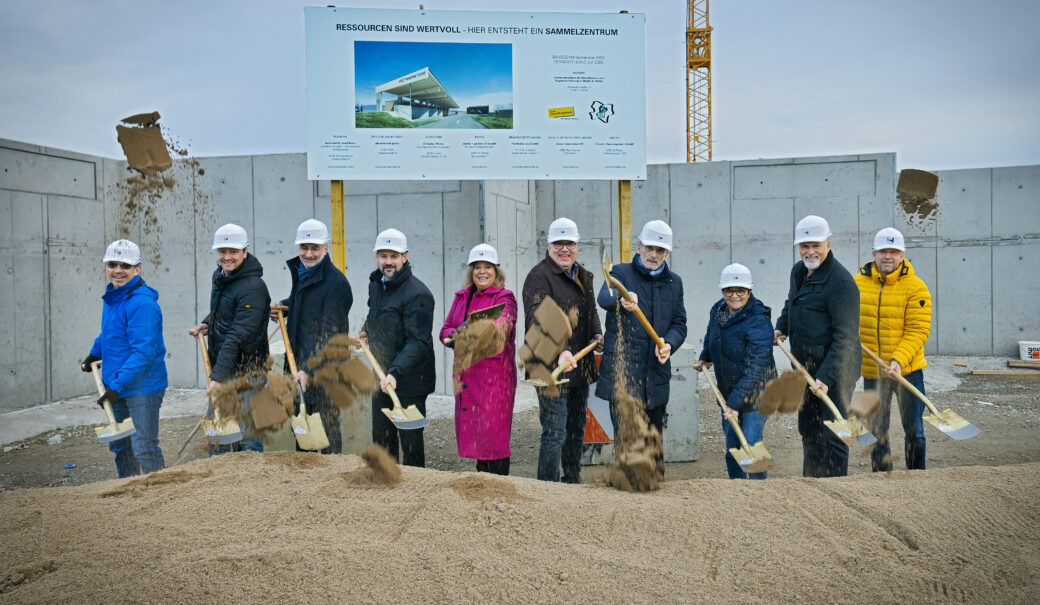 8 Männner, 2 Frauen, stehen mit Schaufeln vor einem Sandhaufen im Hintergrund eine Betonwand, beim Spatenstich für das WSZ Pielachtal Nord